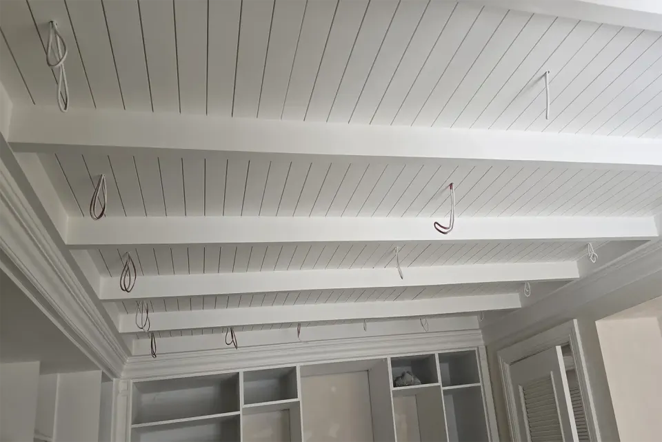 White beamed plank ceiling with lighting cables and shelf niches below
