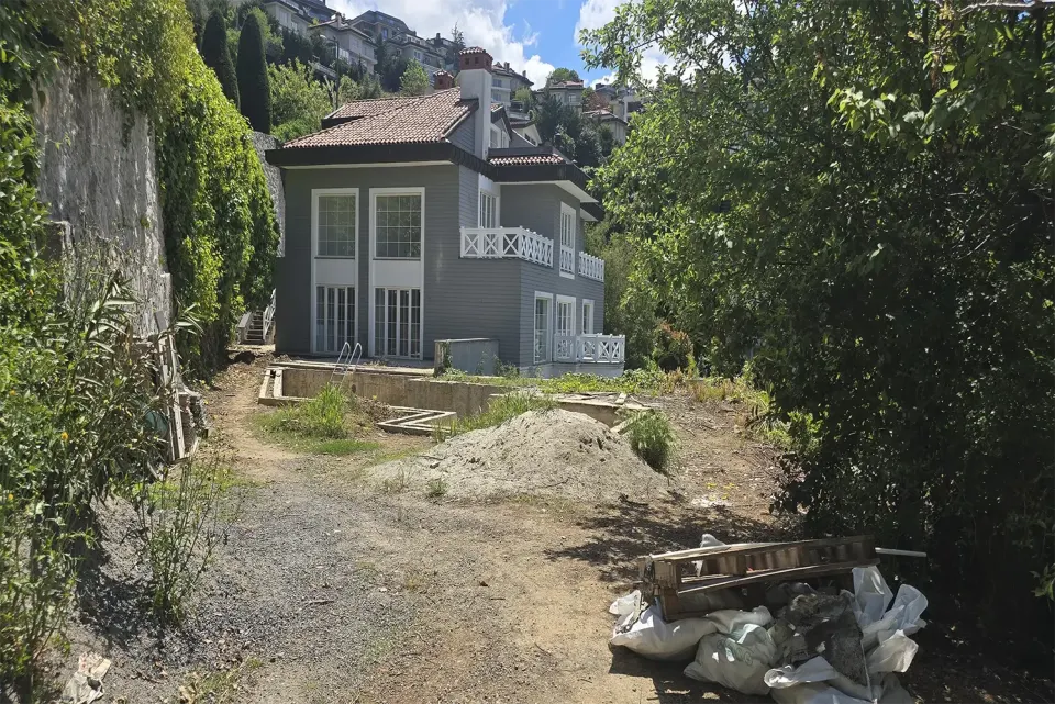 Grey villa seen from the garden path with sand piles and renovation materials