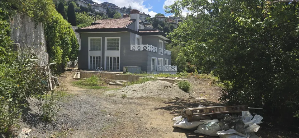 Grey-clad villa exterior with white balcony railings and a garden still under renovation