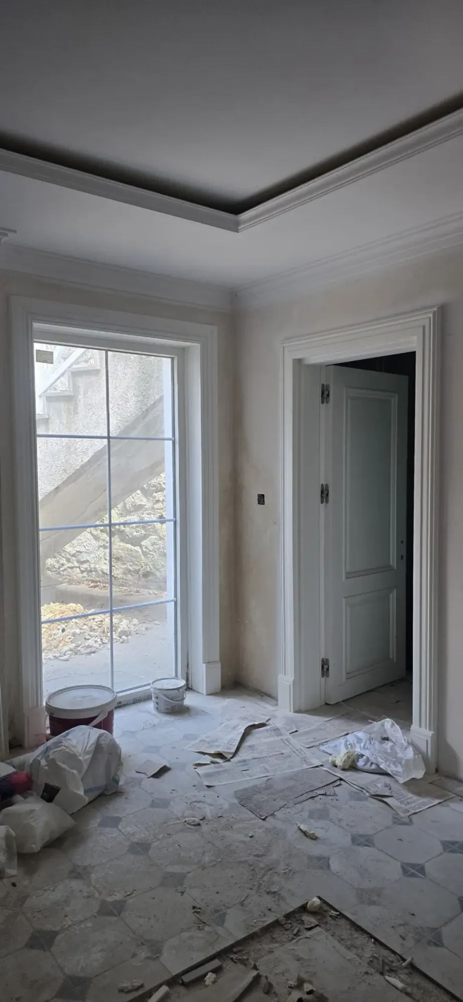 Historic building villa refit in progress with a white panelled interior door, tall window and corniced ceiling