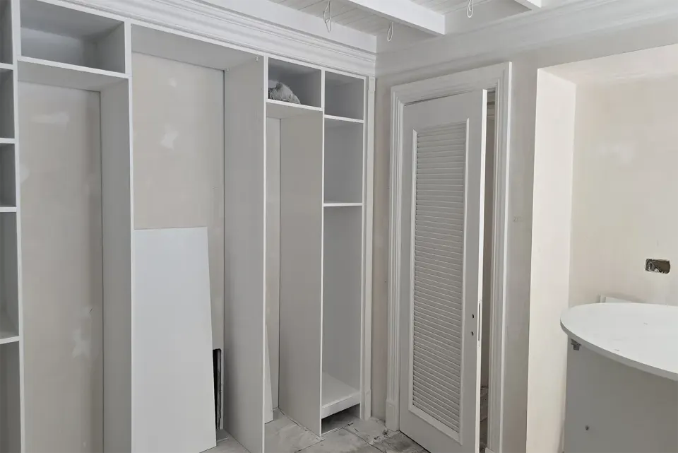 White wardrobe carcass awaiting its doors next to a louvred door
