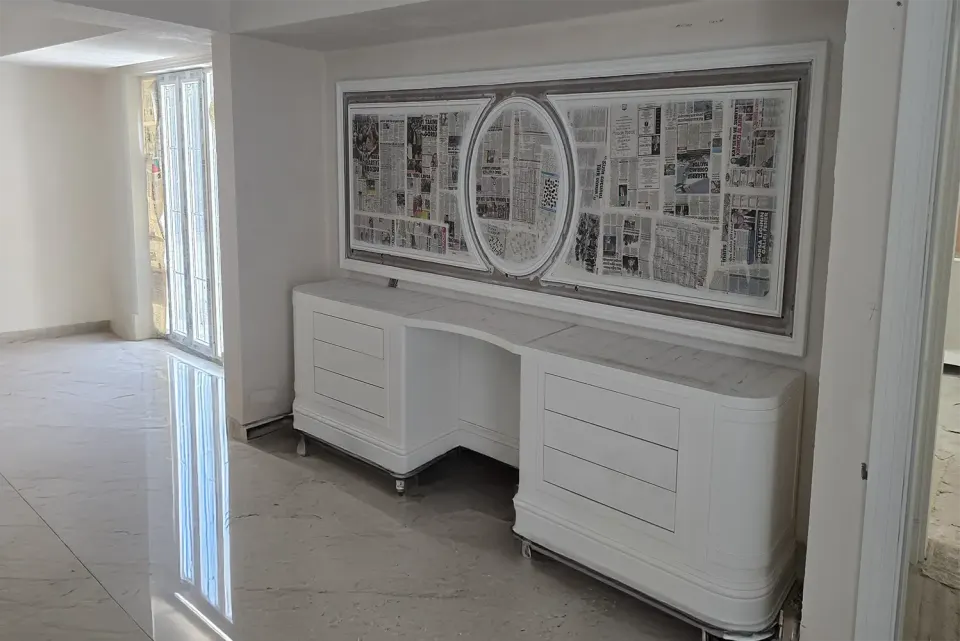 Curved white drawer console with an oval-framed wall panel in a marble hallway