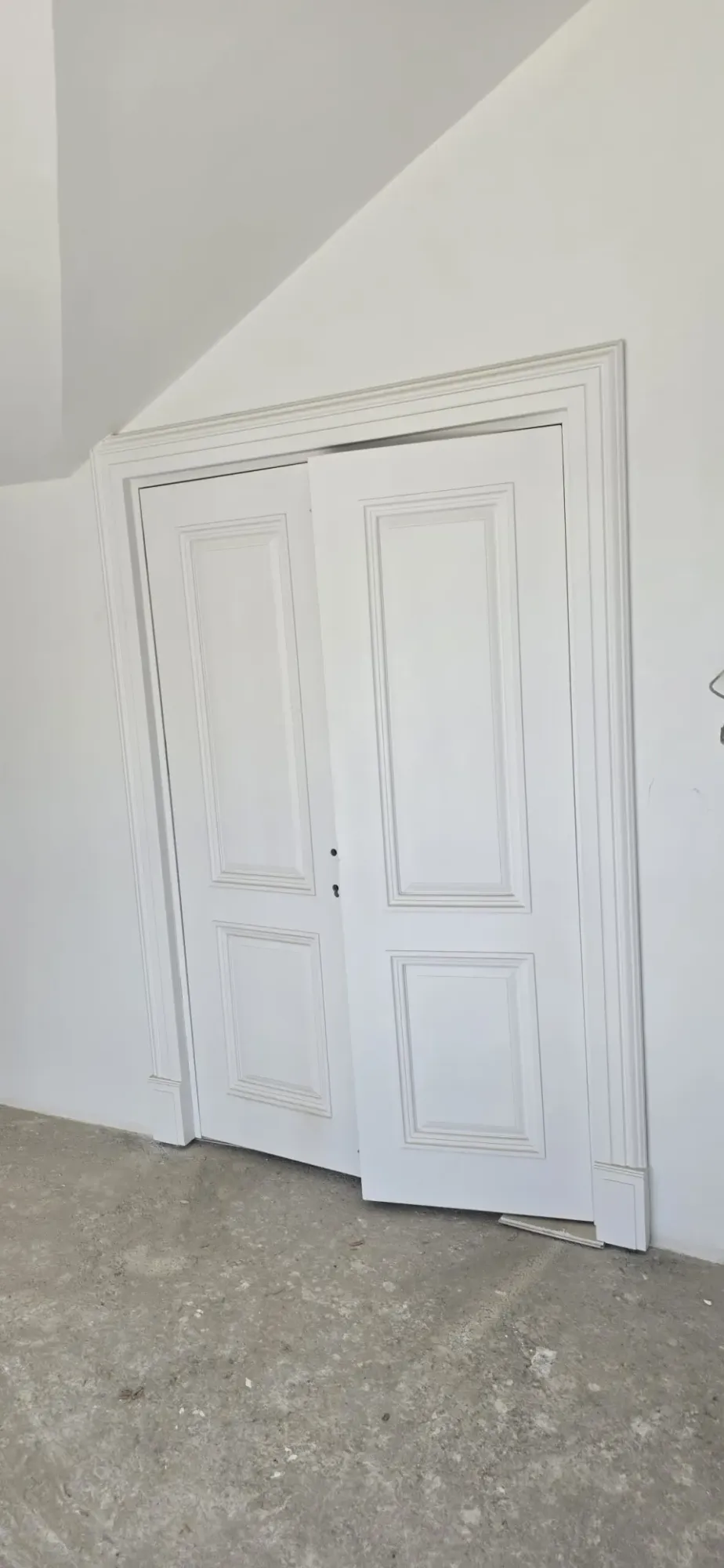 White panelled double interior door with moulded casing under a sloping ceiling