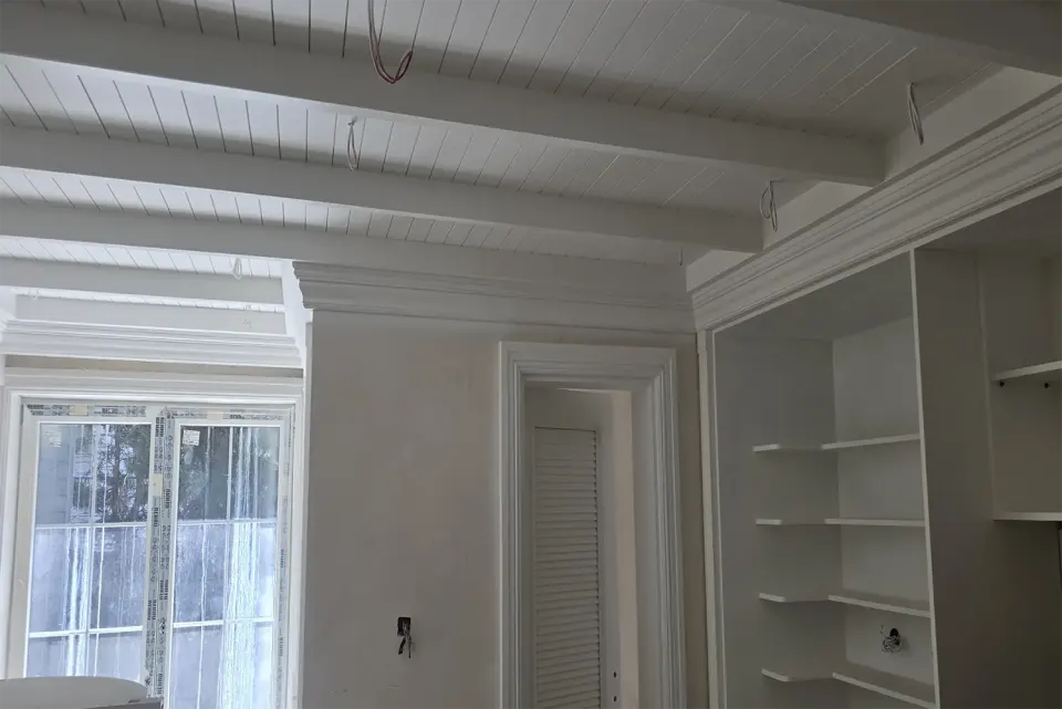 White beamed tongue-and-groove ceiling above built-in shelving and a louvred door
