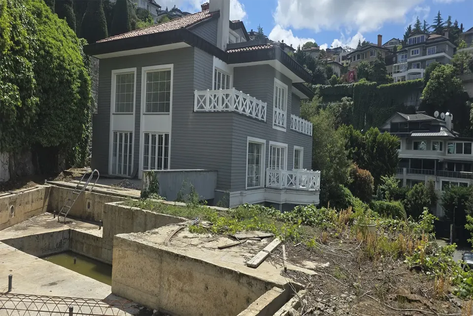 Grey clapboard villa with white cross-pattern balcony railings and an old pool