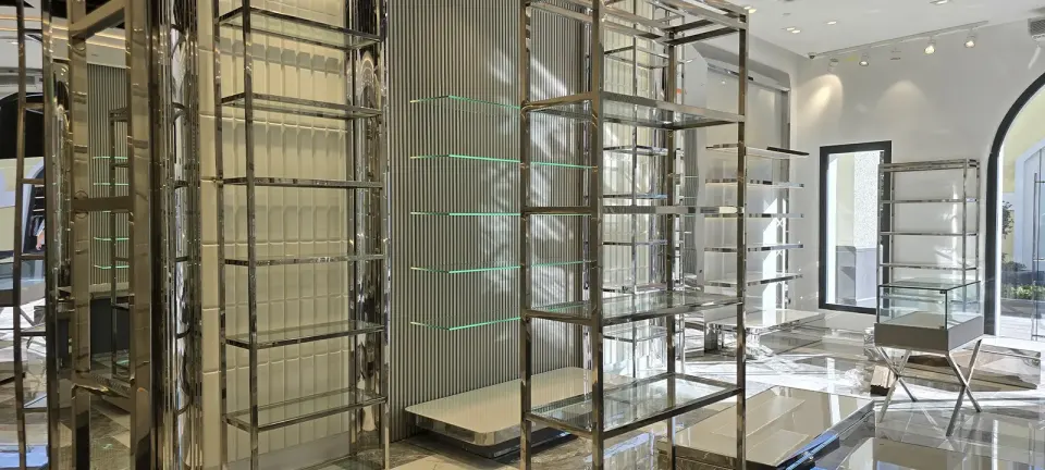 Store shelving system of chrome-framed glass towers with LED-lit wall shelves and an arched doorway