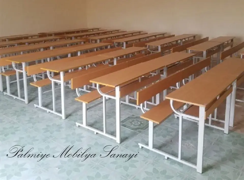 Rows of bench-type school desks with white metal legs lined up in an empty classroom