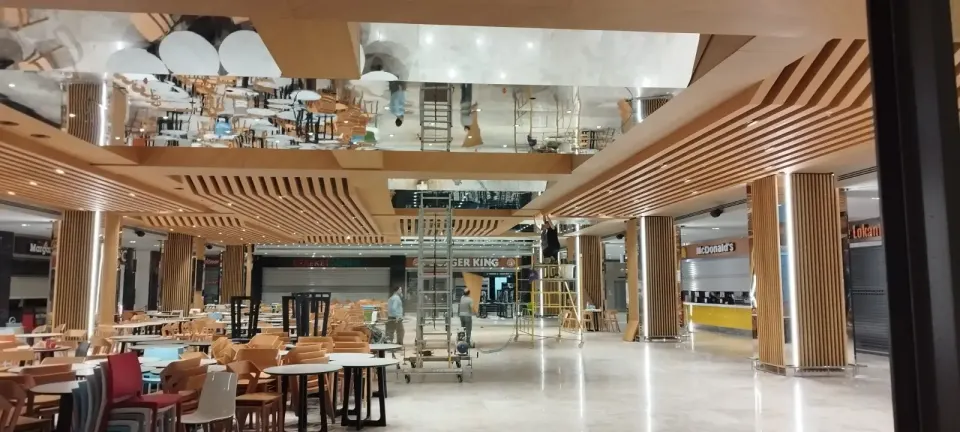 Worker on a scaffold during ceiling fit-out with slat-clad columns and a glossy floor