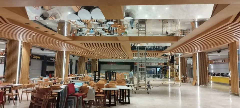 Rolling scaffold and stacked colourful chairs among slat-clad columns during fit-out