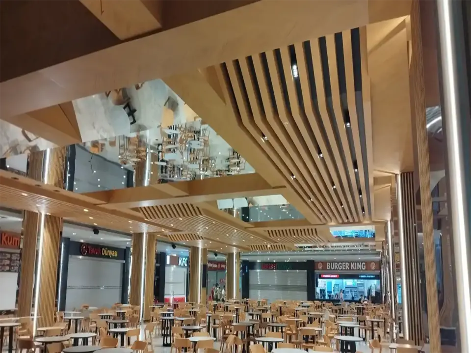 Angled wooden slat beams meeting a mirrored panel above food court counters