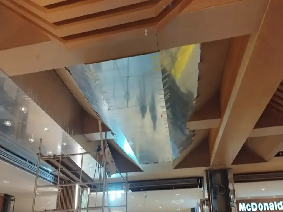 Mirrored ceiling panel being fitted between wooden beams above a scaffold