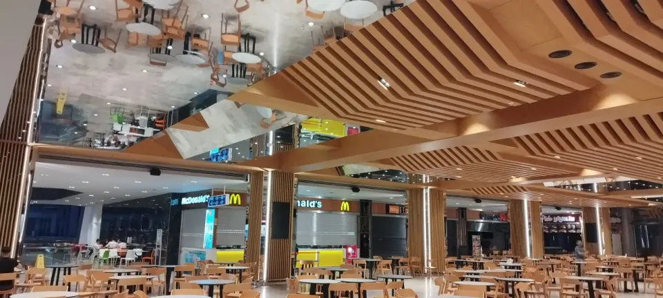 Wide food hall where stepped wooden ceiling slats join the clad columns