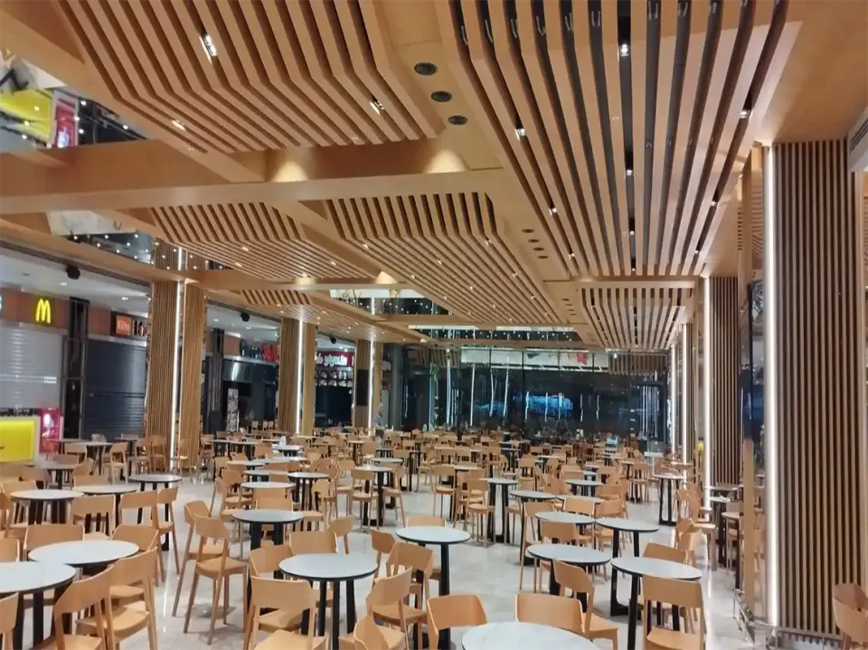 Seating with round white tables under curved wooden slats leading to a glass facade