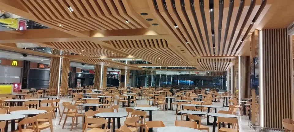 Round tables and wooden chairs set out toward the glazed wall under the slatted ceiling