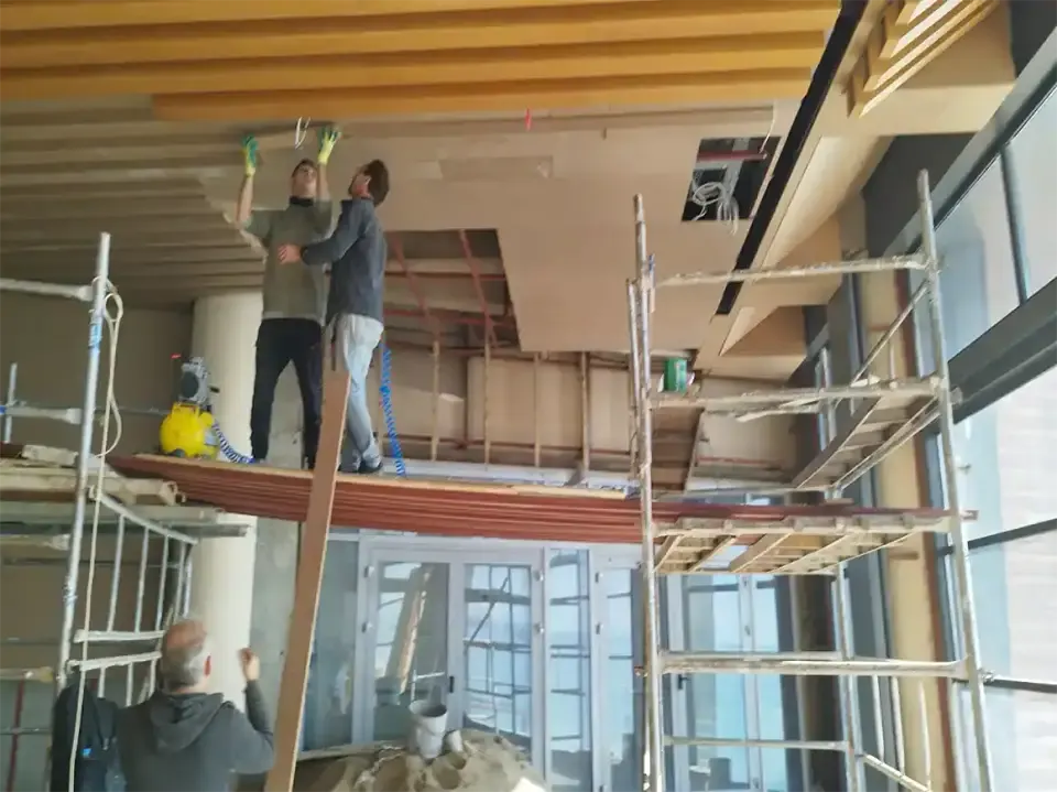 Craftsmen on scaffolding fitting wooden ceiling panels for a hotel interior