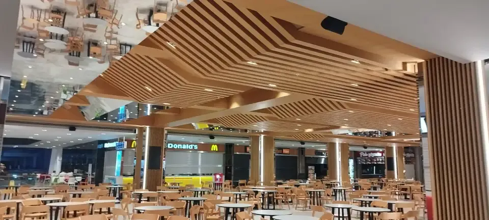 Hotel-style wooden slat ceiling and slatted columns above food court tables and chairs