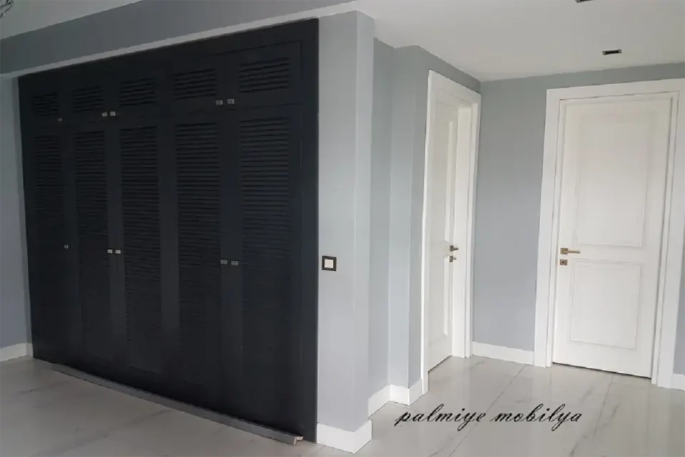 Anthracite louvred built-in wardrobe beside white panelled doors in a grey room