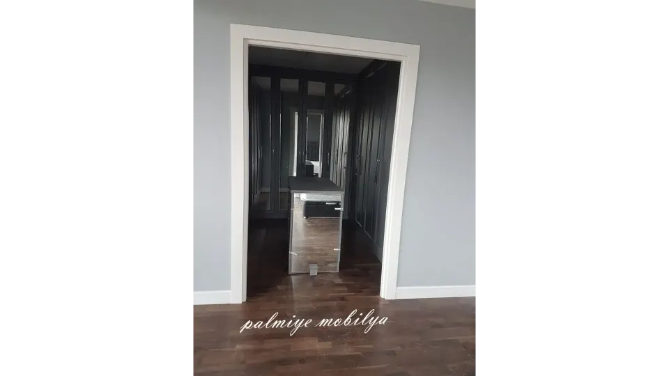 Walk-in closet with dark wardrobes and a mirrored island seen through a white doorway