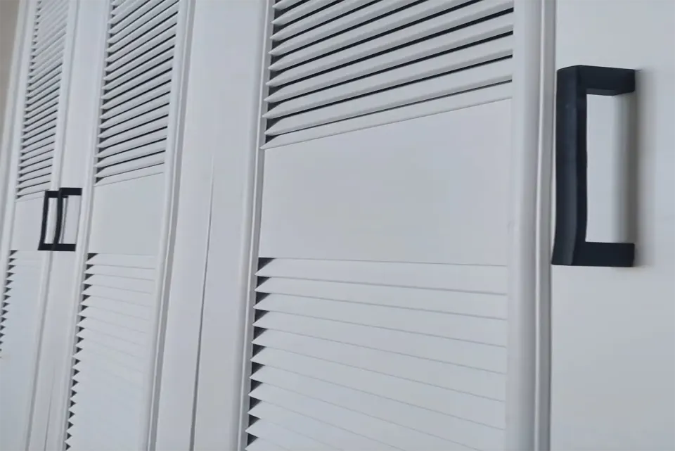 Flat mid-rail panel and chunky black handle on a louvred wardrobe door