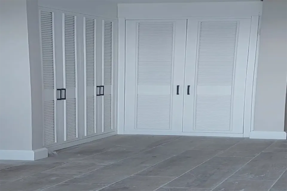 Two louvred wardrobes meeting at the corner of a grey-floored room
