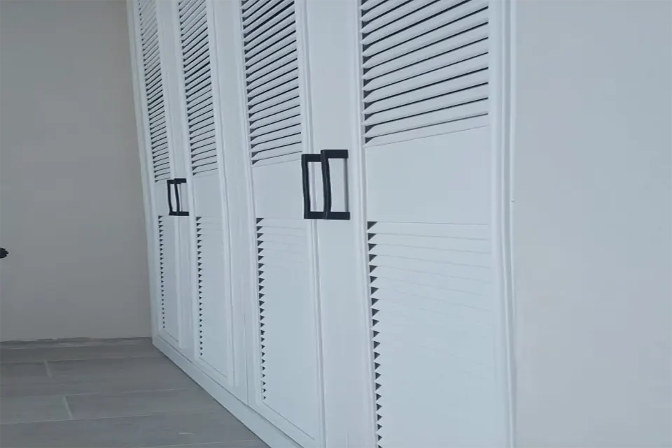 Wall-length white louvred wardrobe in an empty room with grey tiled floor
