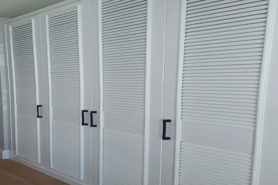 Four-door white louvred wardrobe with black pulls above a wooden floor