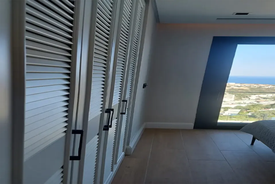 Louvred wardrobe running along a sea-view bedroom beside the tall window