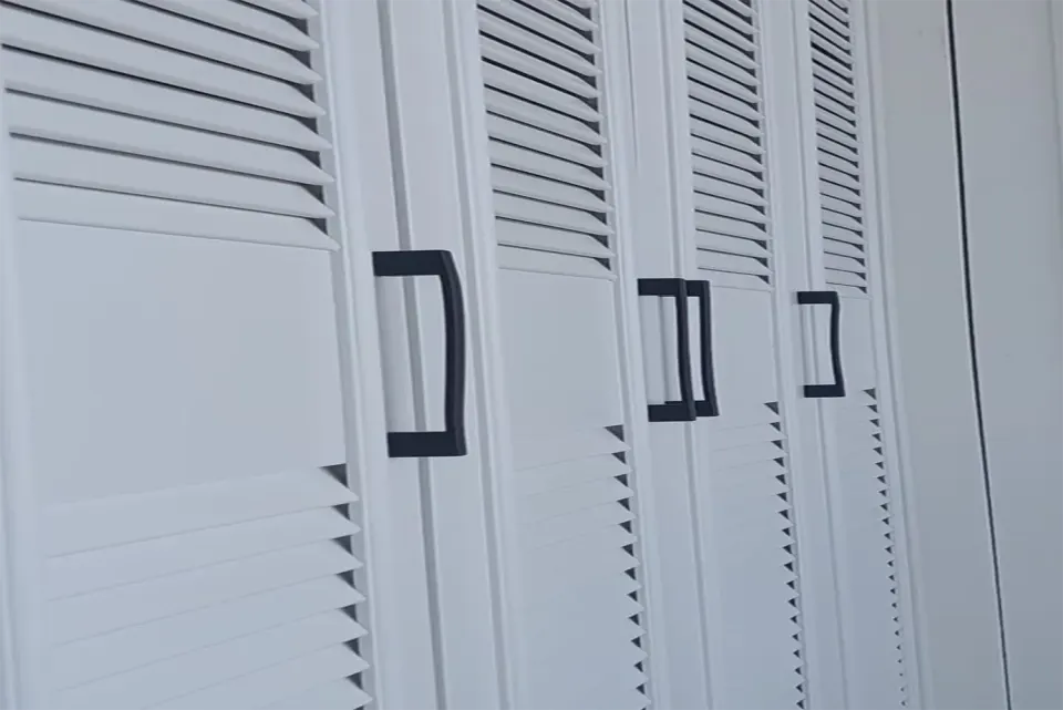 Black metal pulls on white louvred wardrobe doors with horizontal slats