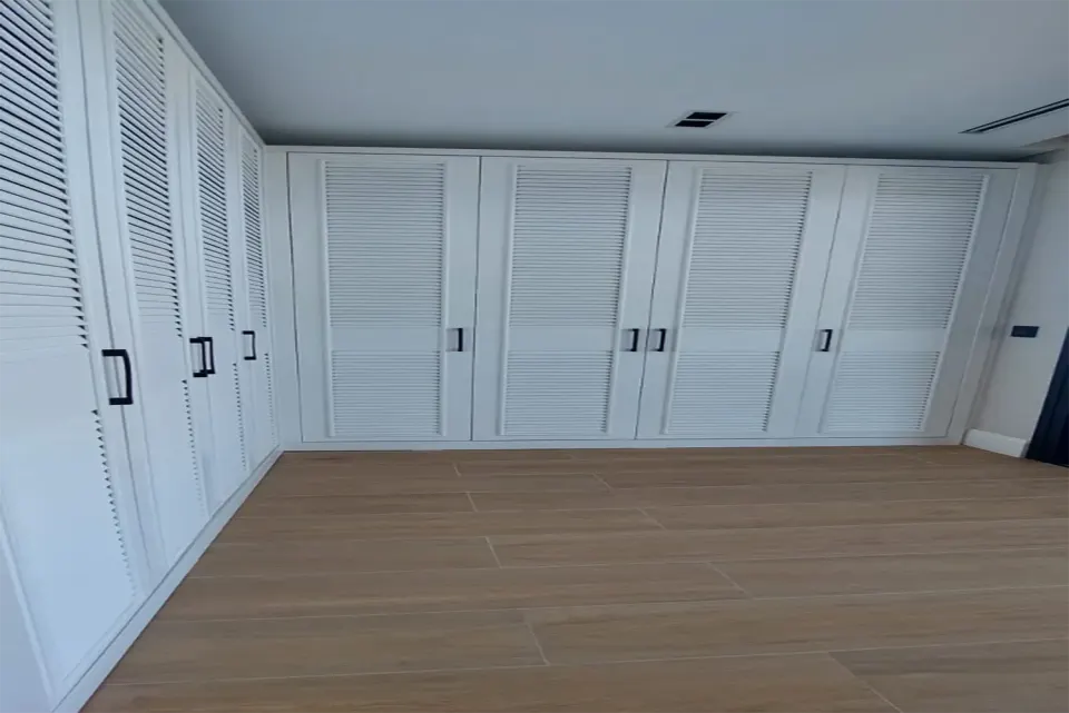 L-shaped louvred wardrobe system lining two walls of a parquet-floored room
