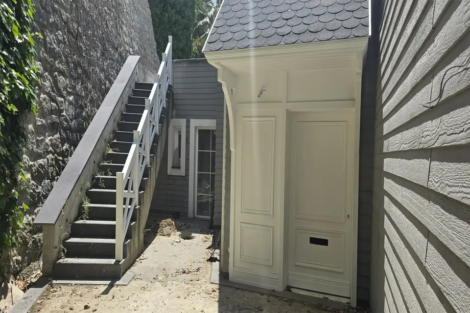 Side courtyard with white-railed stairs beside the shingled canopy entrance