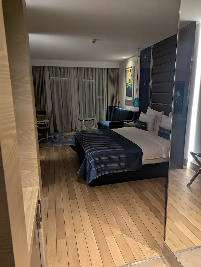 Hotel room furniture with a navy upholstered headboard wall, double bed and light wood floor