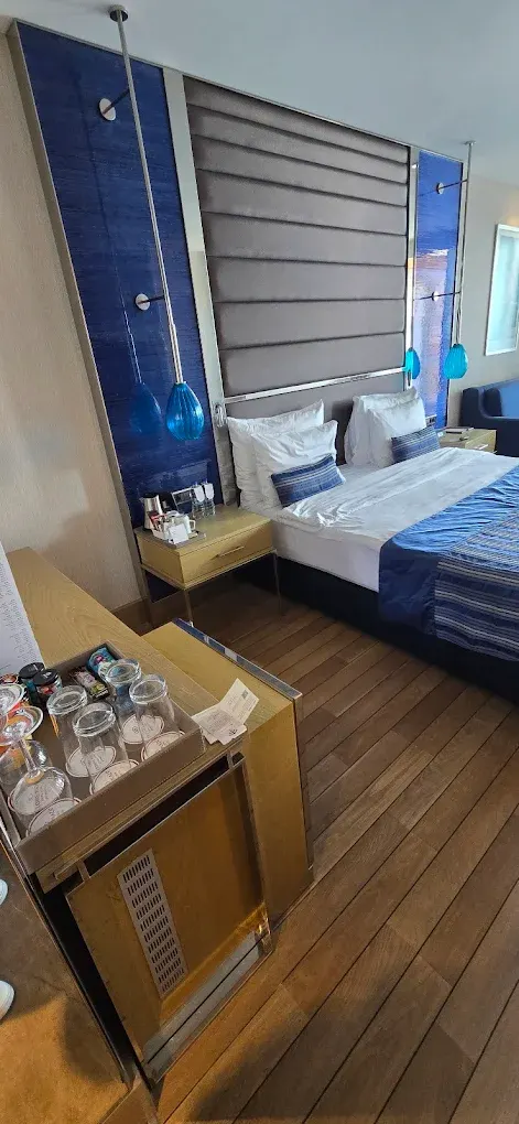 Hotel room with blue padded headboard wall, glass pendant lamps and a wooden minibar unit