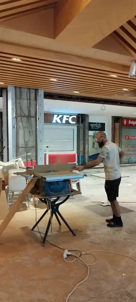 Carpenter cutting boards on a table saw beneath a wooden slat ceiling for hotel furniture